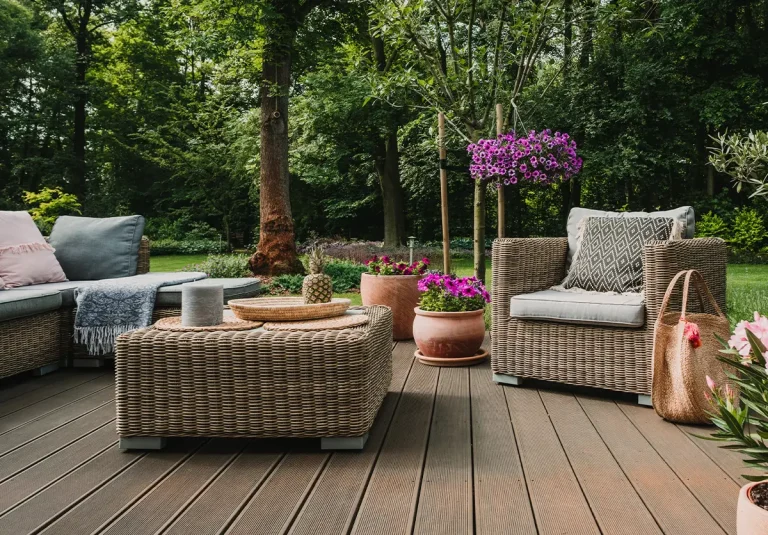Nowoczesne meble ogrodowe z technorattanu na tarasie, zestaw wypoczynkowy z sofą, fotelem i stolikiem, w tle ogród z kwiatami.