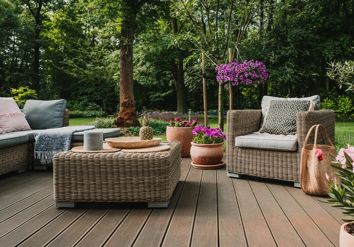 Nowoczesne meble ogrodowe z technorattanu na tarasie, zestaw wypoczynkowy z sofą, fotelem i stolikiem, w tle ogród z kwiatami.
