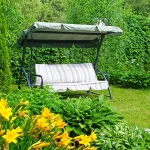 Huśtawka ogrodowa z daszkiem wśród zieleni i kwiatów w przydomowym ogrodzie