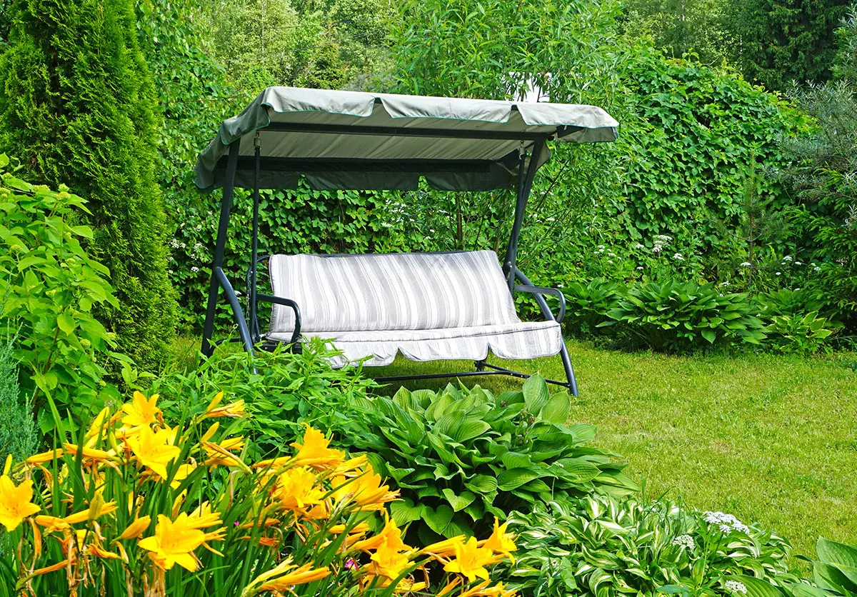 Huśtawka ogrodowa z daszkiem wśród zieleni i kwiatów w przydomowym ogrodzie